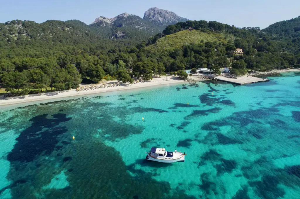 Llaüt-boat in turquoise water with beach and mountains in the background