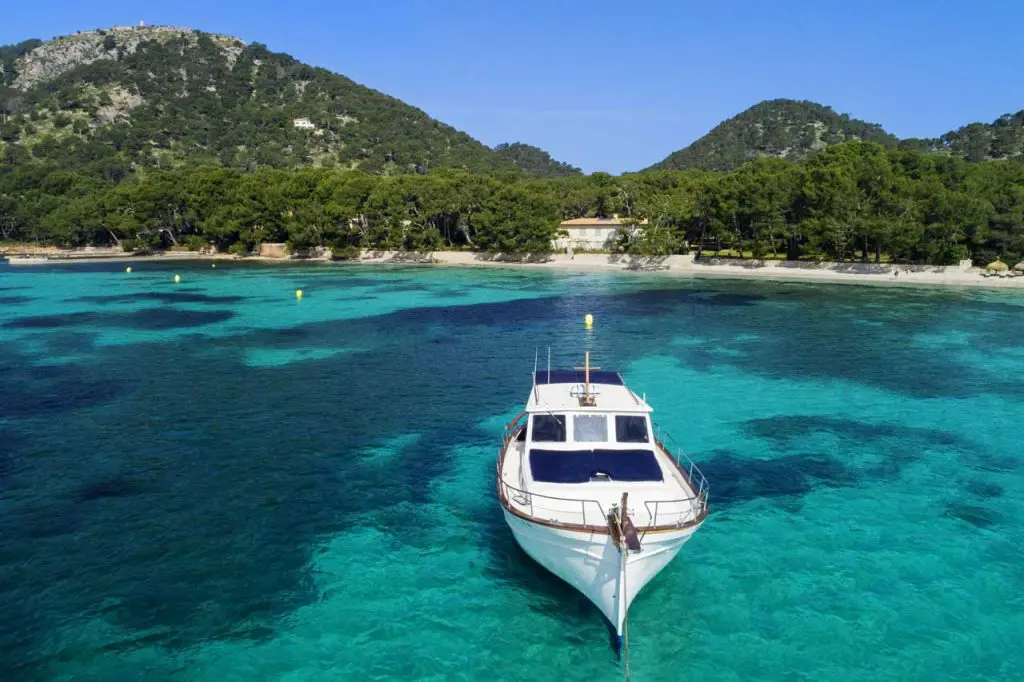 Llaüt-boat in turquoise water with coastline and Tramuntana mountains in the background