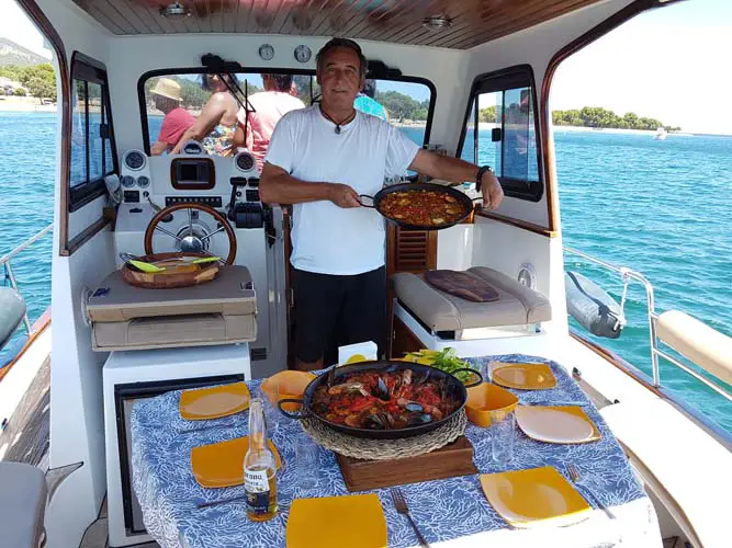 Mann der auf einem Bootsausflug Paella serviert